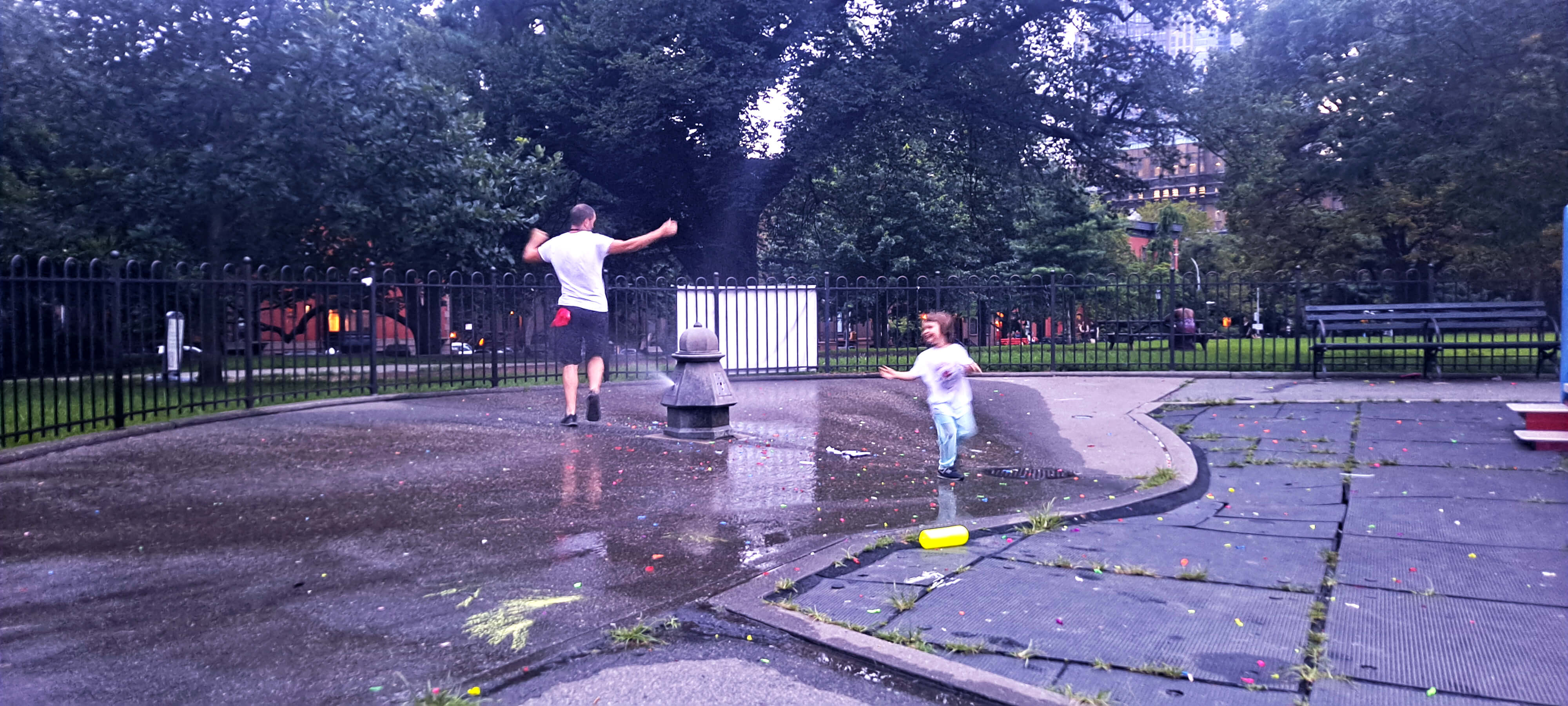 A photo of Alexander Khost and one of his daughter's dancing around a park sprinkler